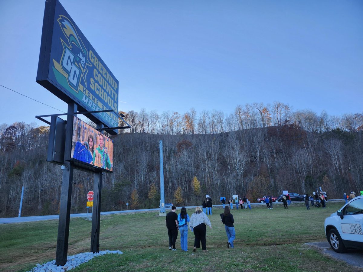 Protestors gather behind the sign for the Greenup County High School and its administrative building where the Board of Education holds their meetings.