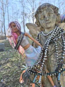Close-up of the angel statue with a Barbie doll, beaded necklaces and a bracelet.

